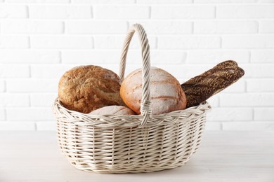 Different types of bread in wicker basket on white wooden table