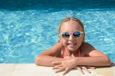 Happy cute little girl with sunglasses at edge of swimming pool on sunny day