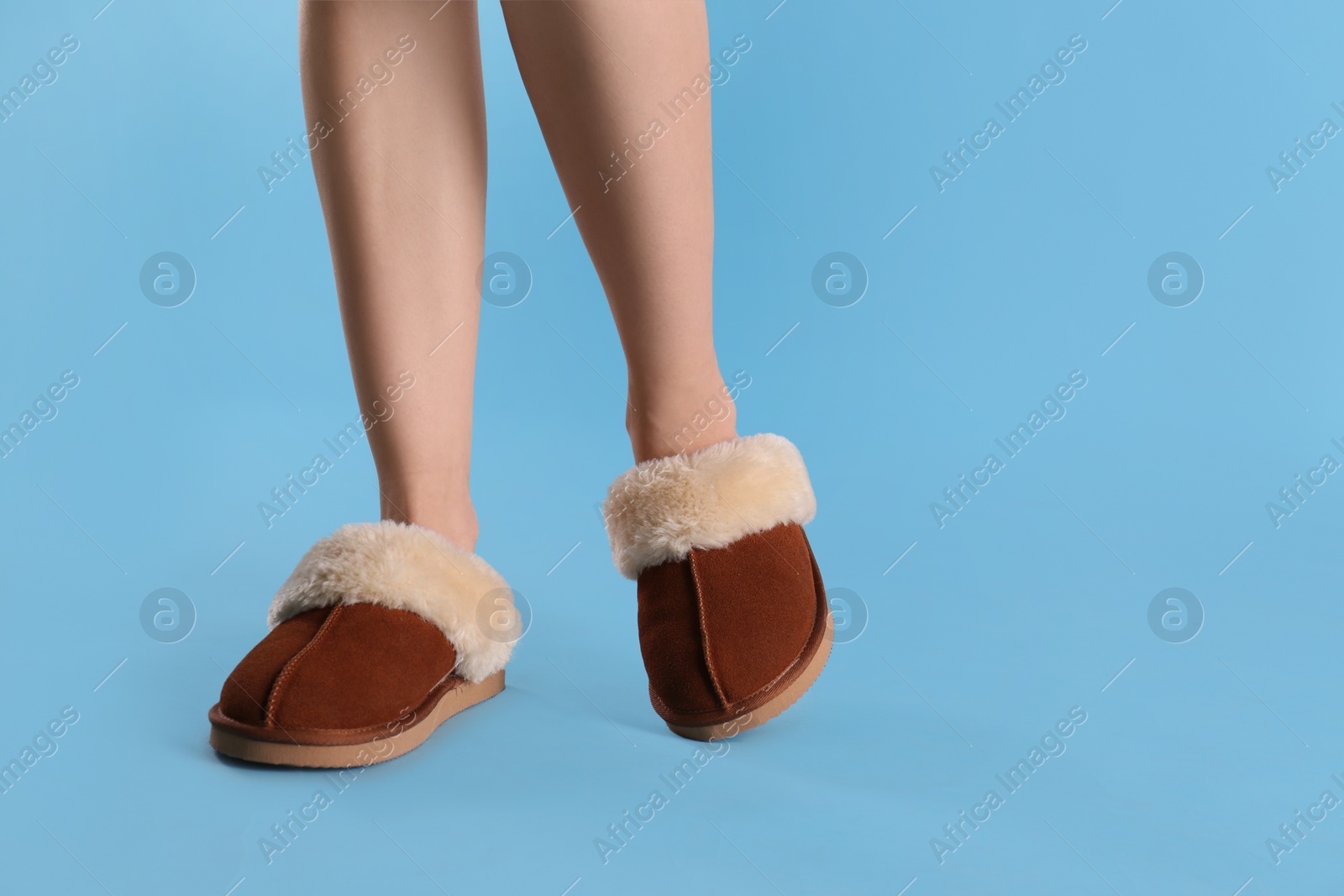 Photo of Woman in warm soft slippers on light blue background, closeup. Space for text