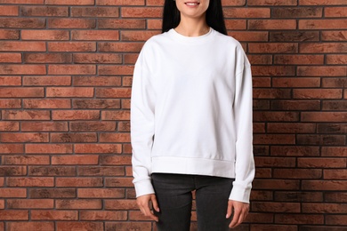 Photo of Young woman in sweater at brick wall, closeup. Mock up for design