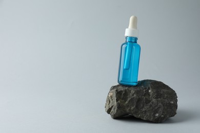 Photo of Bottle of cosmetic serum on stone against light grey background, space for text