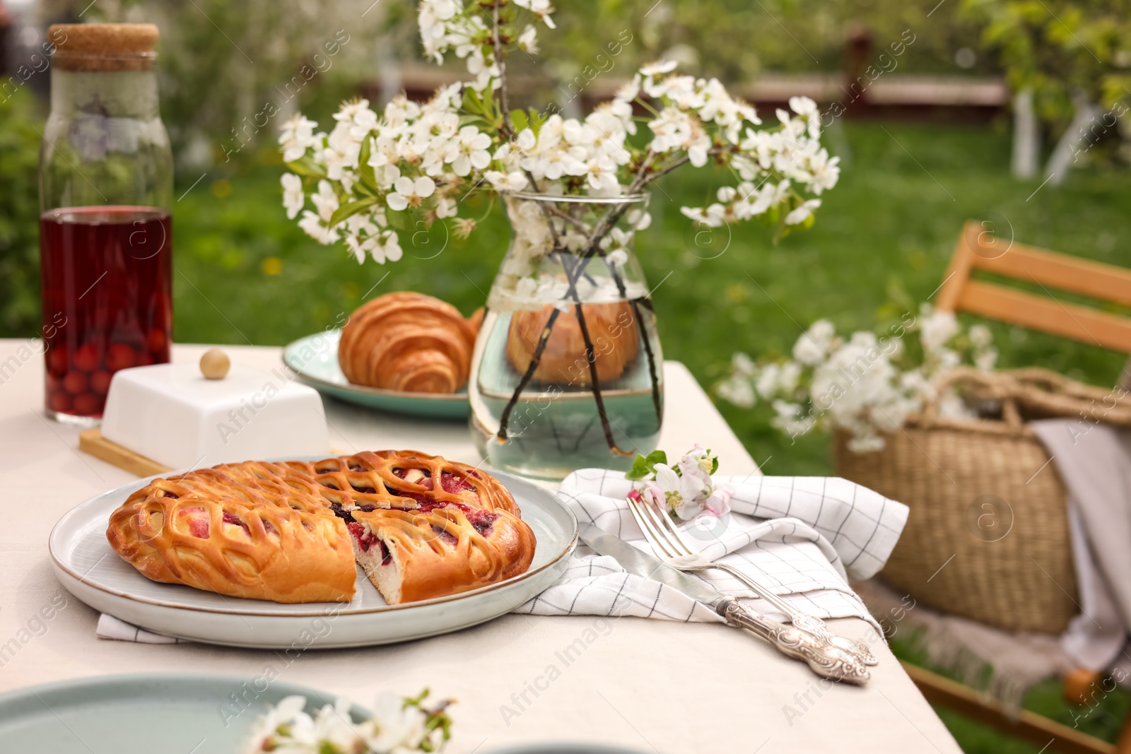 Photo of Stylish table setting with beautiful spring flowers, fruit drink and pie in garden