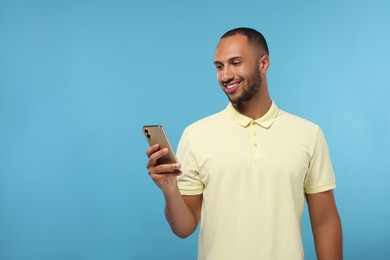 Photo of Happy man sending message via smartphone on light blue background, space for text