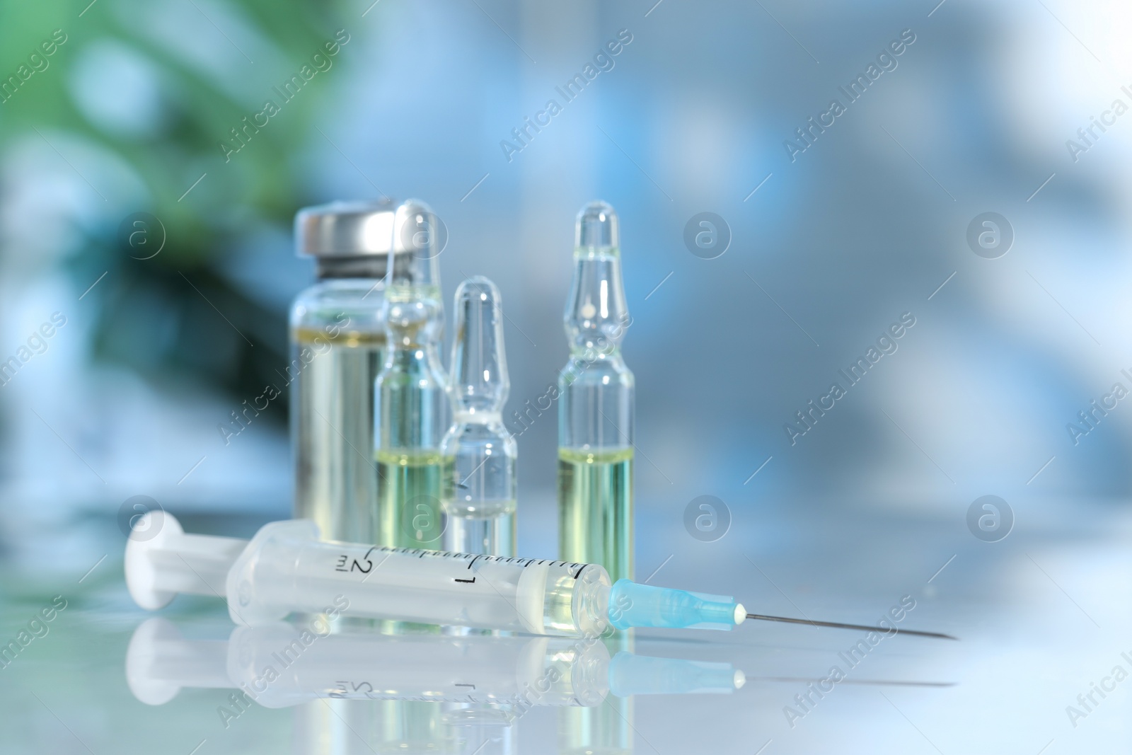 Photo of Glass vial, ampoules and syringe on white table, closeup. Space for text