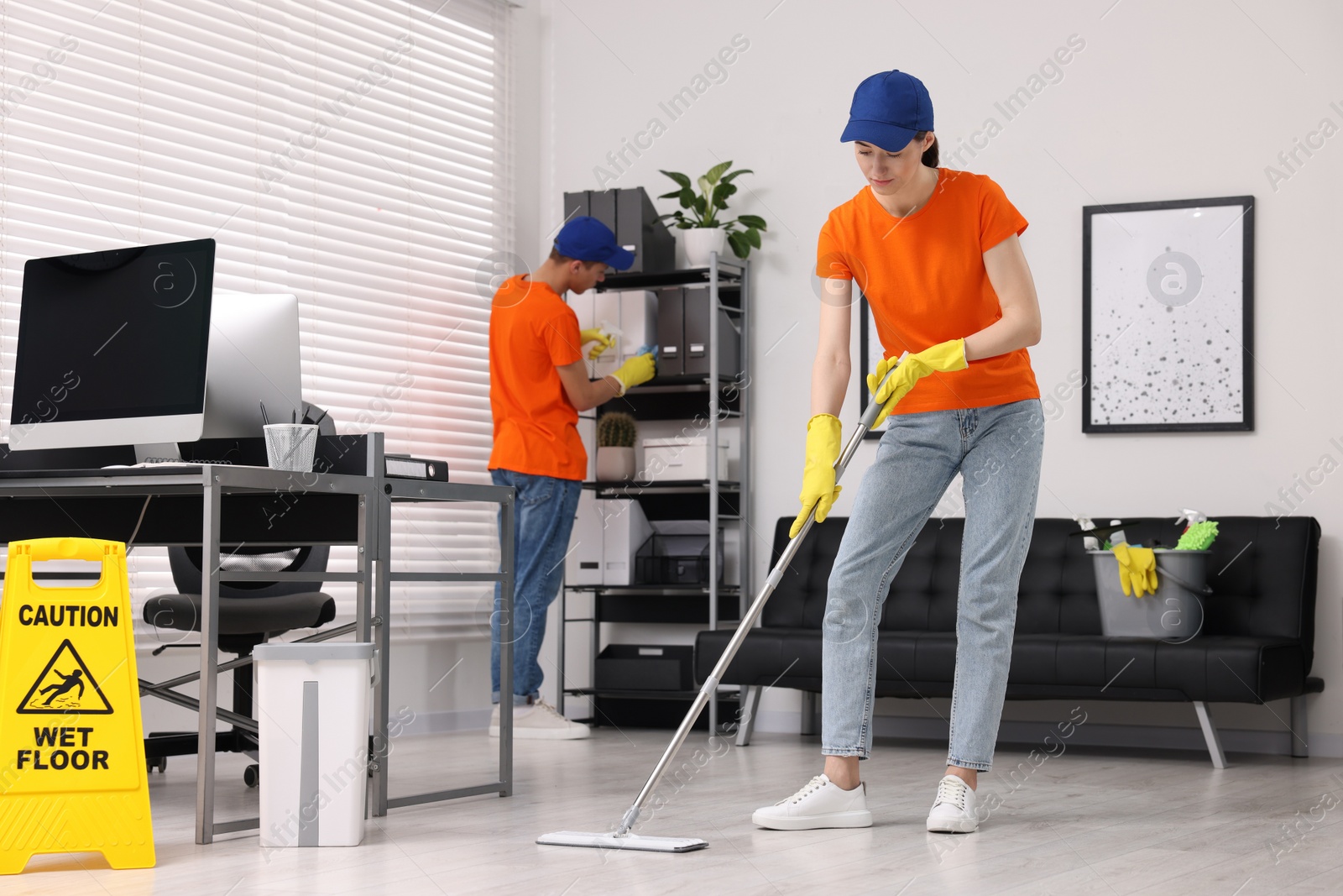 Photo of Cleaning service workers cleaning. Bucket with supplies and wet floor sign in office