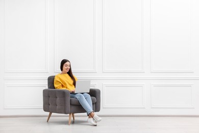 Photo of Beautiful woman with laptop sitting in armchair near white wall indoors, space for text
