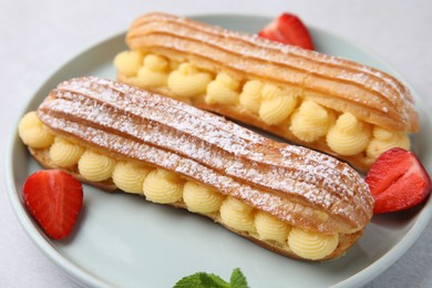 Photo of Delicious eclairs filled with cream and strawberries on table, closeup