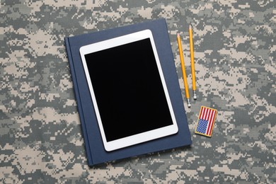 Photo of Notebook, tablet, pencils and patch on camouflage background, flat lay. Military education