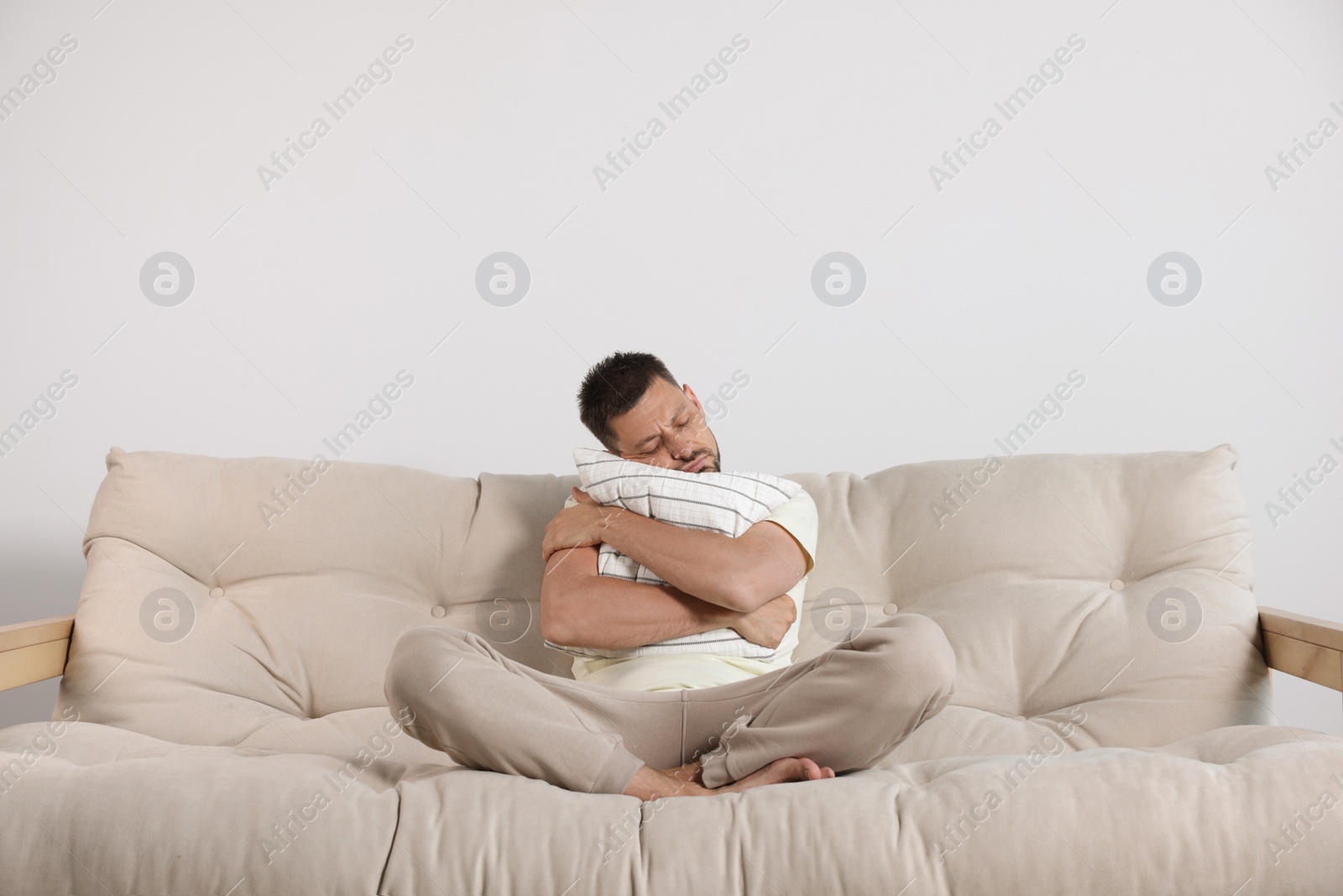 Photo of Sleepy man hugging pillow on sofa at home