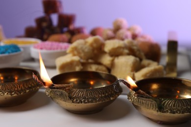 Happy Diwali. Diya lamps on white table against violet background, closeup