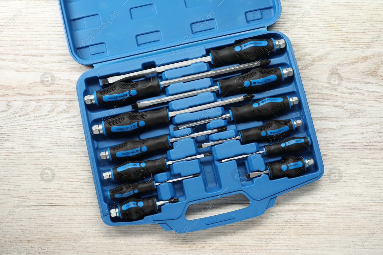 Photo of Set of screwdrivers in open toolbox on light wooden table, top view