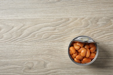 Photo of Open tin can of beans on wooden background, top view. Space for text