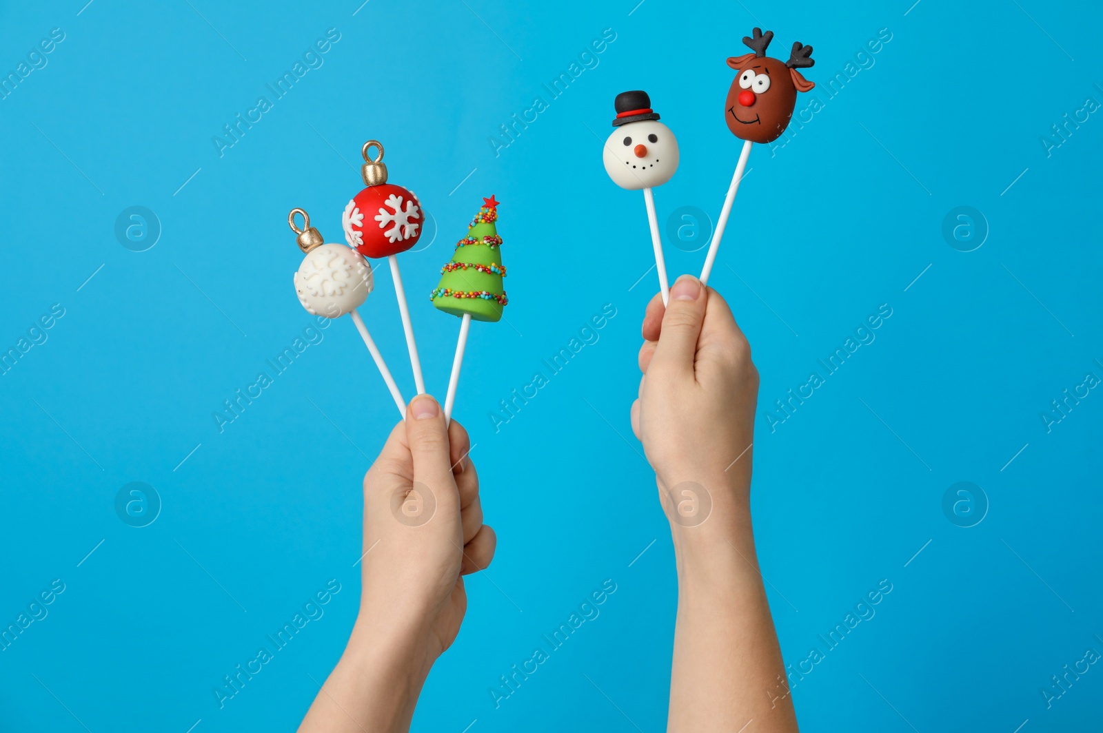 Photo of Woman holding delicious Christmas themed cake pops against light blue background, closeup