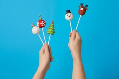 Woman holding delicious Christmas themed cake pops against light blue background, closeup
