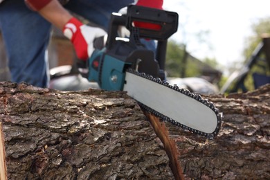 Photo of Man sawing wooden log outdoors, selective focus