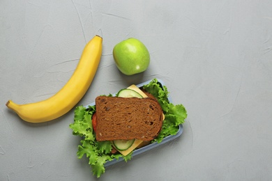 Photo of Lunch box with tasty sandwich and fruits on grey background, top view