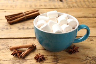 Photo of Tasty hot chocolate with marshmallows and spices on wooden table, closeup