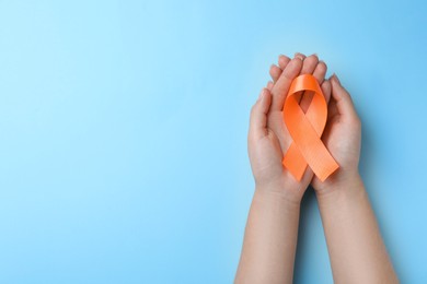 Photo of Woman holding orange ribbon on light blue background, top view with space for text. Multiple sclerosis awareness