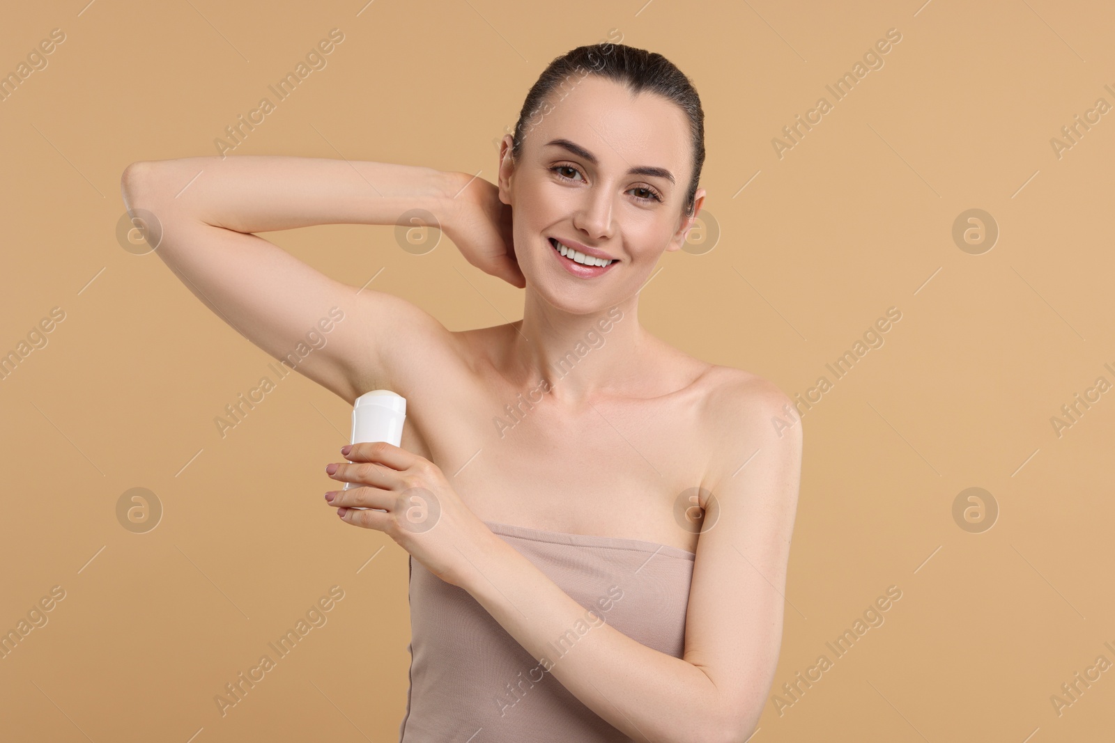 Photo of Beautiful woman applying deodorant on beige background