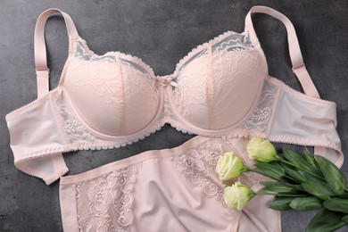 Elegant beige plus size women's underwear and beautiful eustoma flowers on grey background, flat lay
