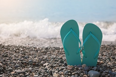 Photo of Stylish turquoise flip lops on pebble beach near sea, closeup. Space for text