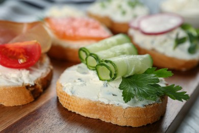 Photo of Toasted bread with cream cheese, cucumber and parsley on wooden board, closeup