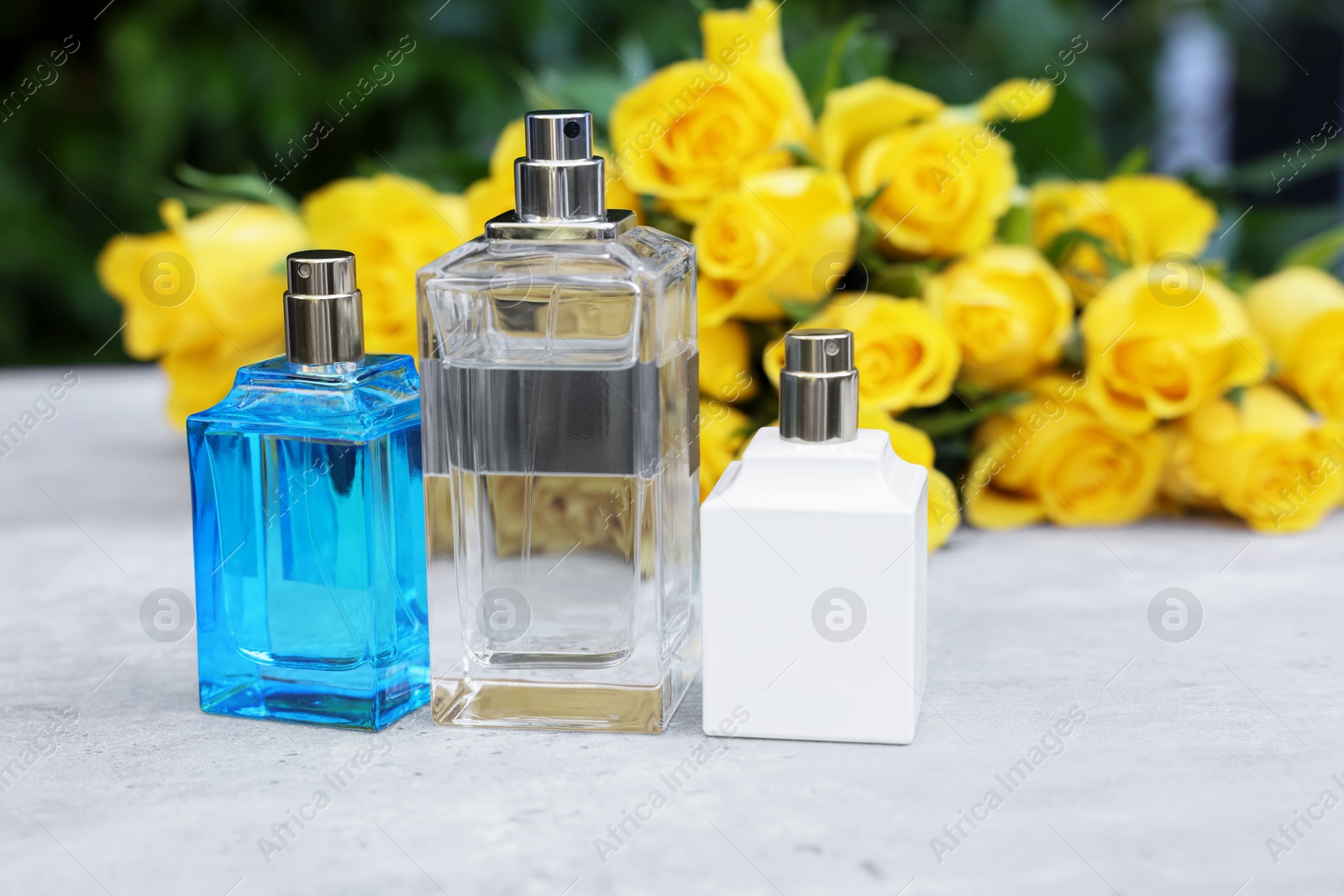 Photo of Perfumes and beautiful bouquet of yellow roses on light table outdoors, selective focus. Space for text