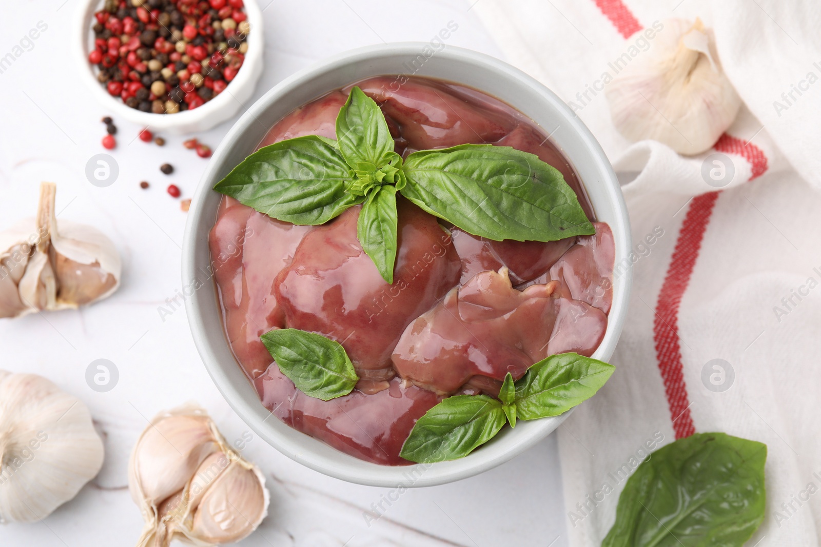 Photo of Bowl with raw chicken liver, garlic, peppercorns and basil on white textured table, flat lay