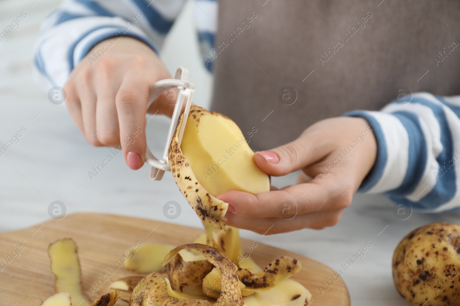 Photo of Woman peeling fresh potato at white marble table, closeup