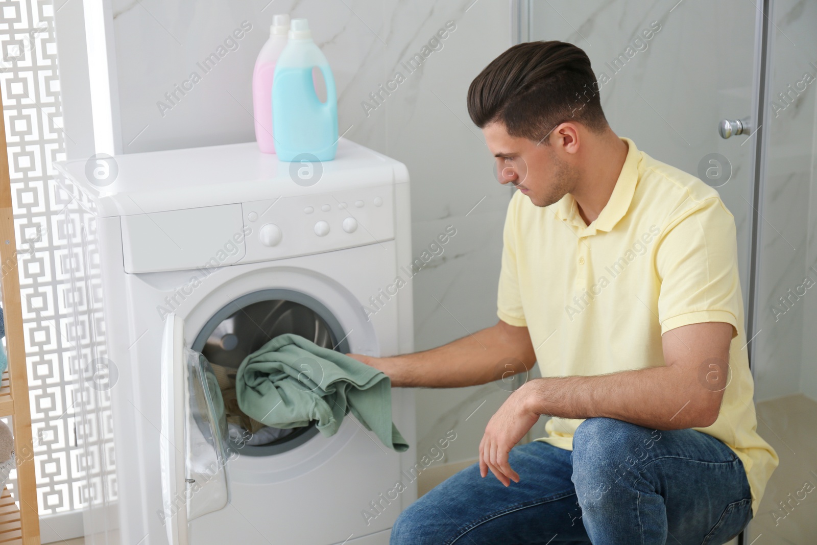 Photo of Man putting clothes into washing machine in bathroom. Laundry day