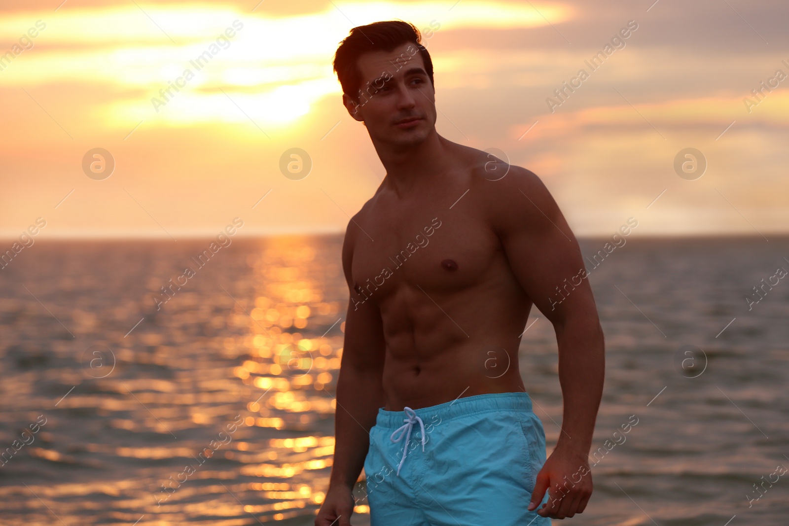 Photo of Handsome young man posing on beach near sea at sunset