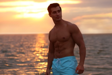 Handsome young man posing on beach near sea at sunset