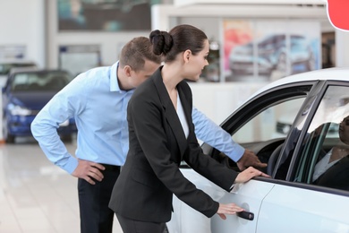 Photo of Young saleswoman working with client in car dealership