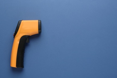 Infrared thermometer on blue background, top view with space for text. Checking temperature during Covid-19 pandemic