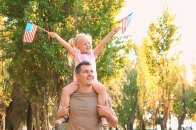 Photo of Man holding his daughter with American flags in park on sunny day