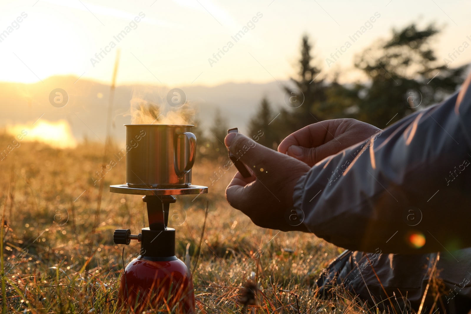 Photo of Man making hot drink with portable gas burner in mountain camping, closeup