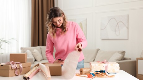 Beautiful young woman wrapping gift at table in living room