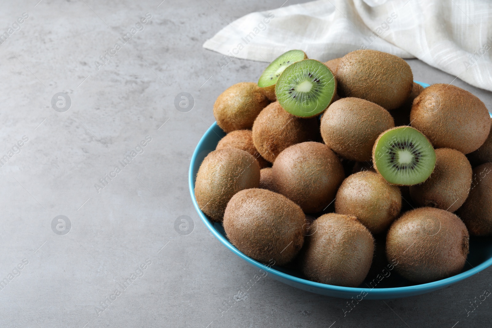 Photo of Fresh ripe kiwis in bowl on light grey table, space for text