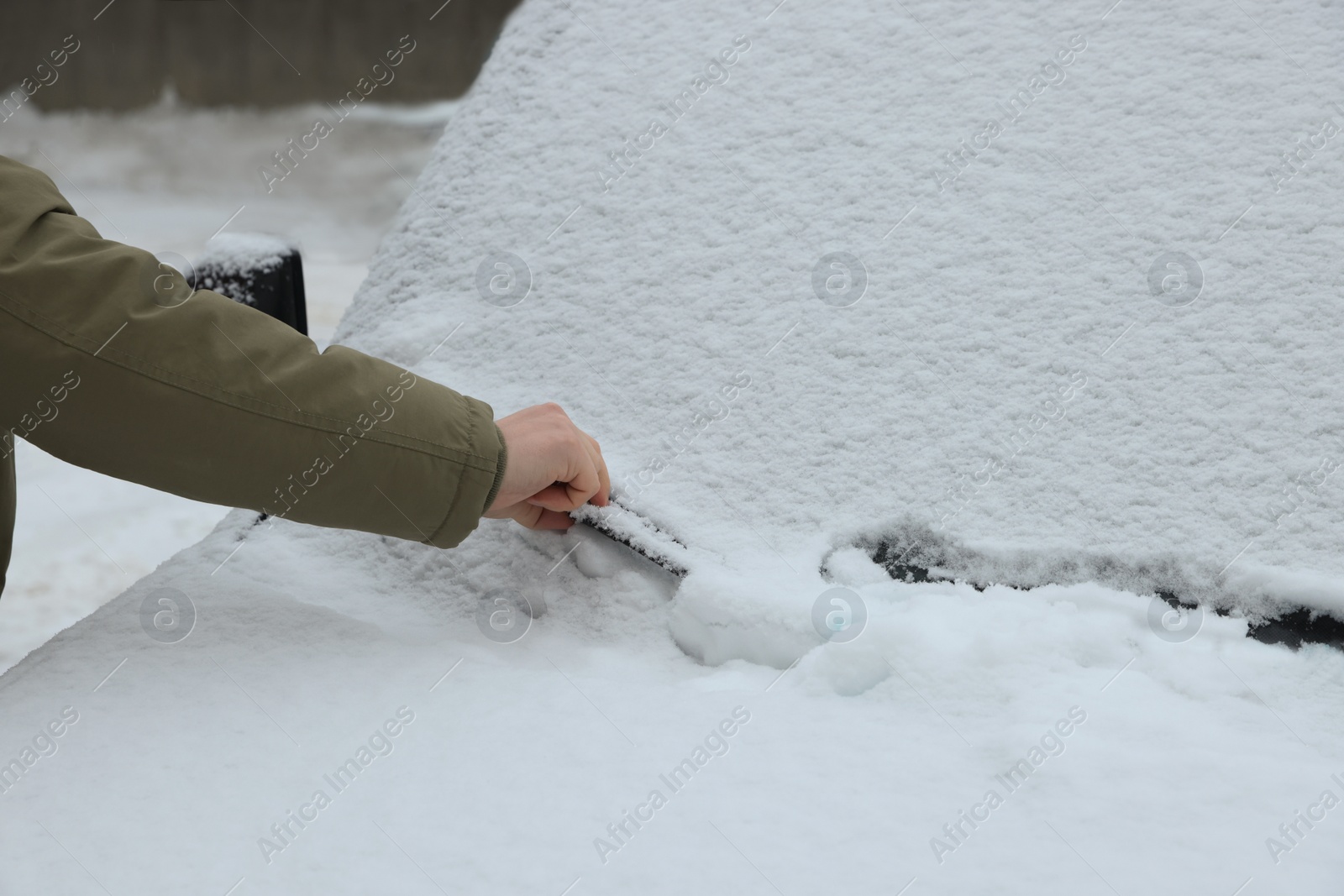 Photo of Woman cleaning car wiper blade covered with snow outdoors, closeup