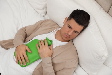 Man with hot water bottle sleeping on bed