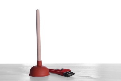 Photo of Plunger with wooden handle and pipe wrench on white table