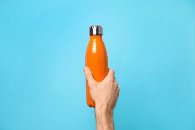 Photo of Man holding orange thermos bottle on light blue background, closeup