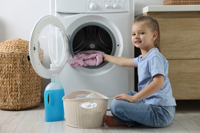 Little girl putting dirty clothes into washing machine in bathroom