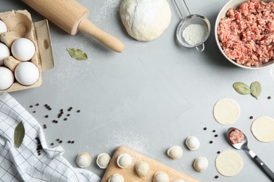 Photo of Flat lay composition with raw dumplings and ingredients on grey background, space for text. Process of cooking