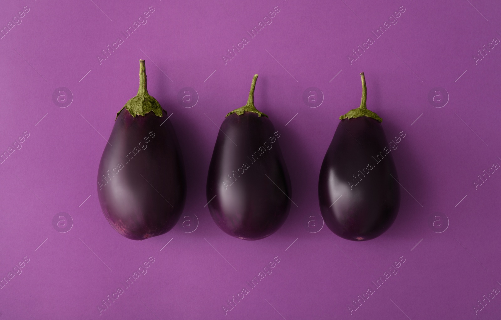 Photo of Raw ripe eggplants on purple background, flat lay