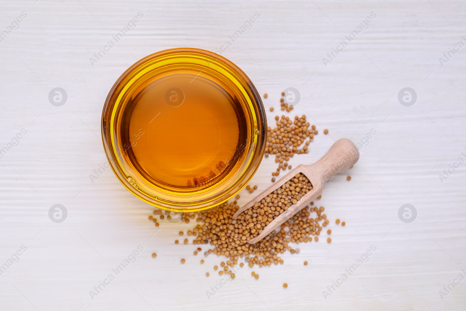 Bowl of natural oil and scoop with mustard seeds on white wooden table, flat lay Photo of Bowl of natural oil and scoop with mustard seeds on white wooden table, flat lay
