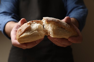 Photo of Man breaking loaf of fresh bread on dark background, closeup