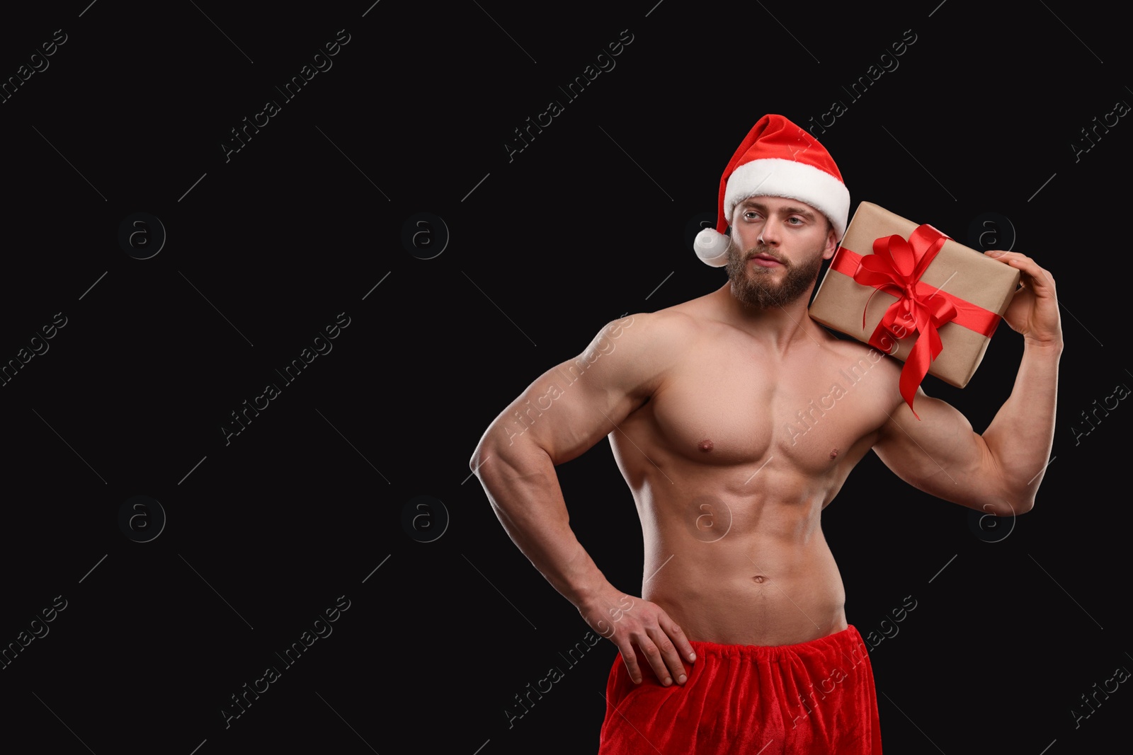 Photo of Attractive young man with muscular body holding Christmas gift box on black background, space for text