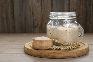 Photo of Leaven and ears of wheat on beige wooden table, space for text