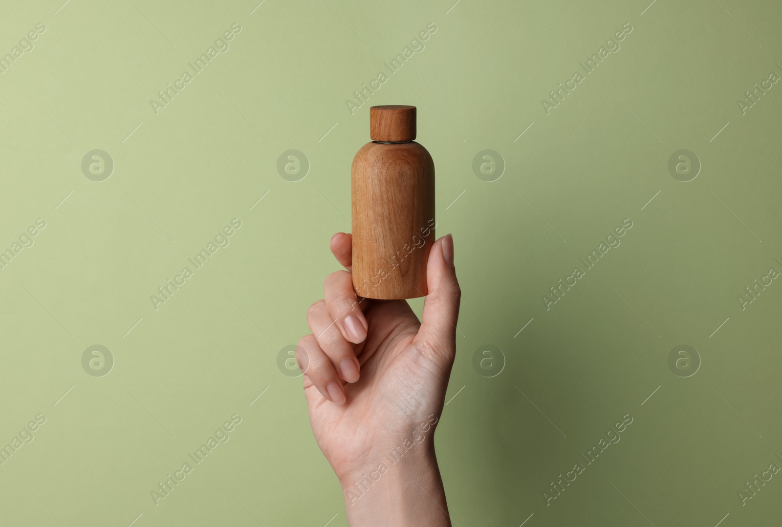 Photo of Woman holding bottle of cosmetic product on pale olive background, closeup. Space for text